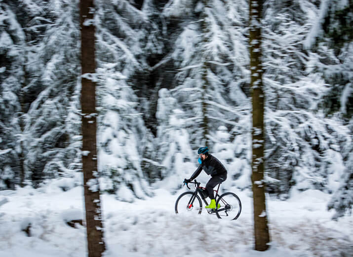 Ein Radfahrer fährt im Wald, im Hintergrund liegt Schnee. Ein Radfahrer fährt im Wald, im Hintergrund liegt Schnee.
