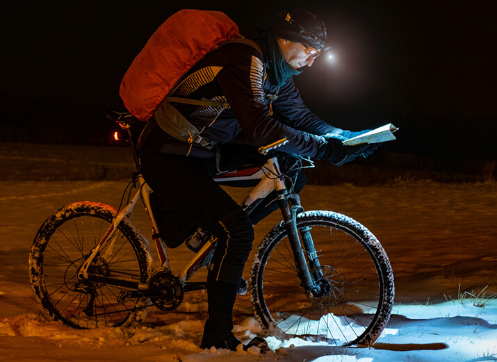Ein Radfahrer studiert im Winter eine Karte mit einer Helmlampe. Ein Radfahrer studiert im Winter eine Karte mit einer Helmlampe.