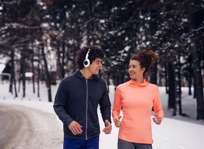 Eine Frau und ein Mann in Sportklamotten joggen langsam auf einem verschneiten Pfad. Eine Frau und ein Mann in Sportklamotten joggen langsam auf einem verschneiten Pfad.